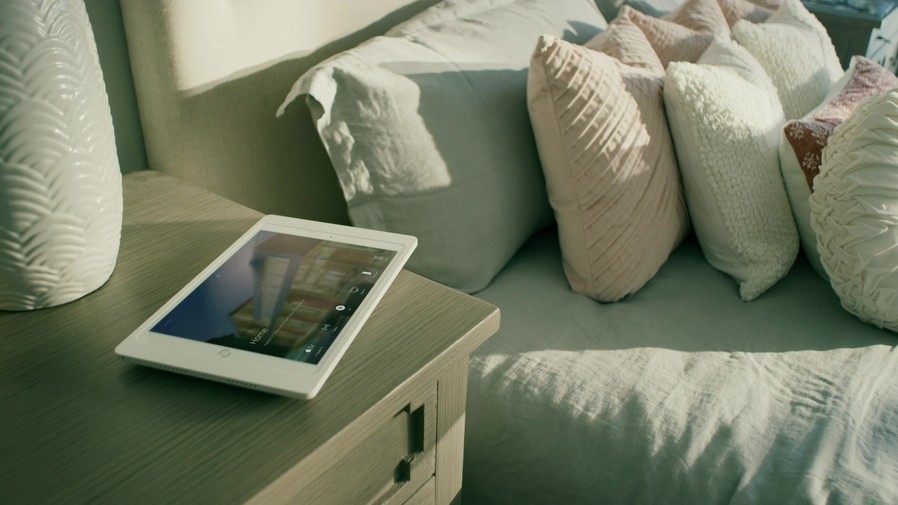 Savant touchscreen on a bedside table. The interface shows the Savant platform’s Home menu.