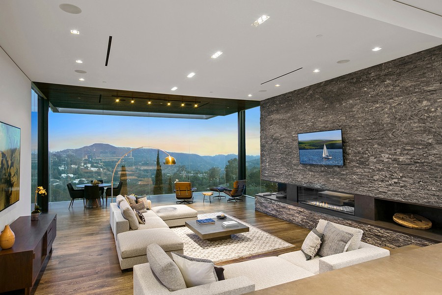 A living area with floor-to-ceiling windows, in-ceiling speakers, and a TV above a fire feature.