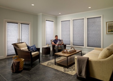 A man sitting in his living room with multiple windows around him featuring lowered automatic blinds.