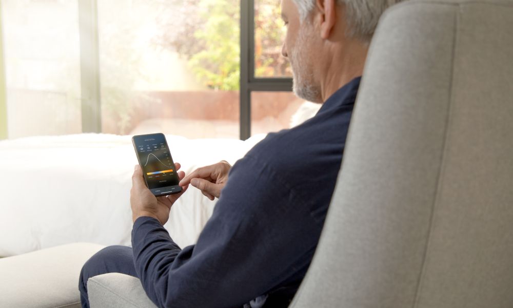 Man seated in a grey confortable chair looking the Savant Power App in his phone